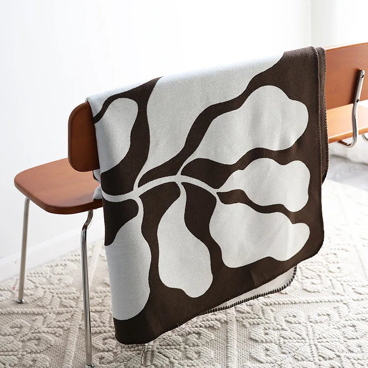 Mocha and grey abstract jacquard blanket draped over a wooden chair on a textured cream rug