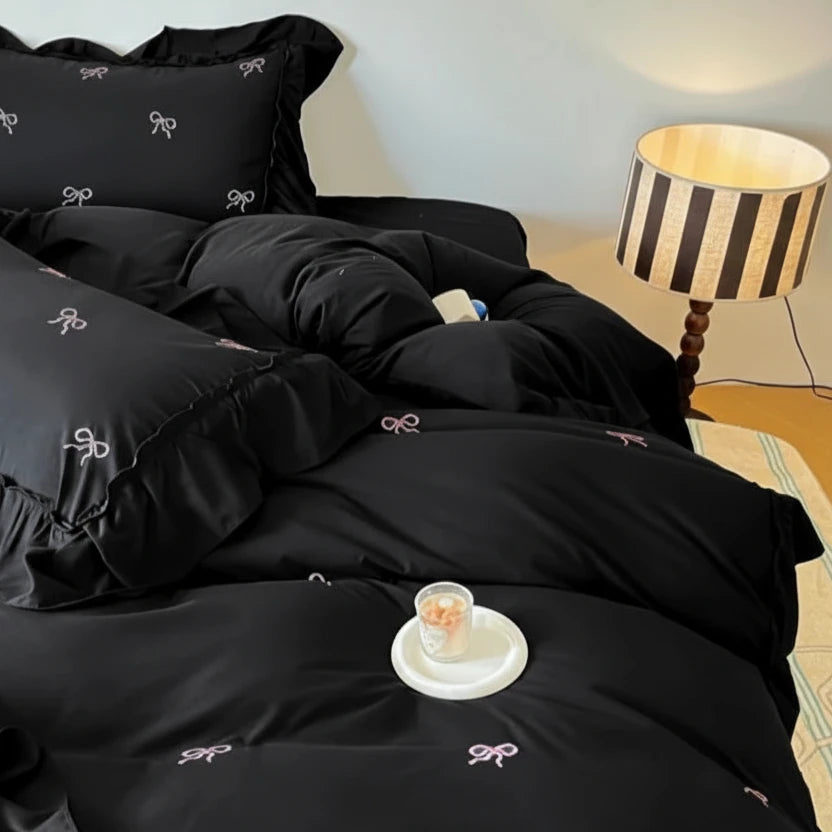 Black bedding set with bow patterns on a bed in a bedroom.