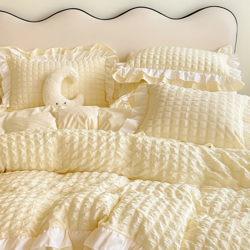 Yellow textured comforter set on a bed with a lamp and plant in the background.