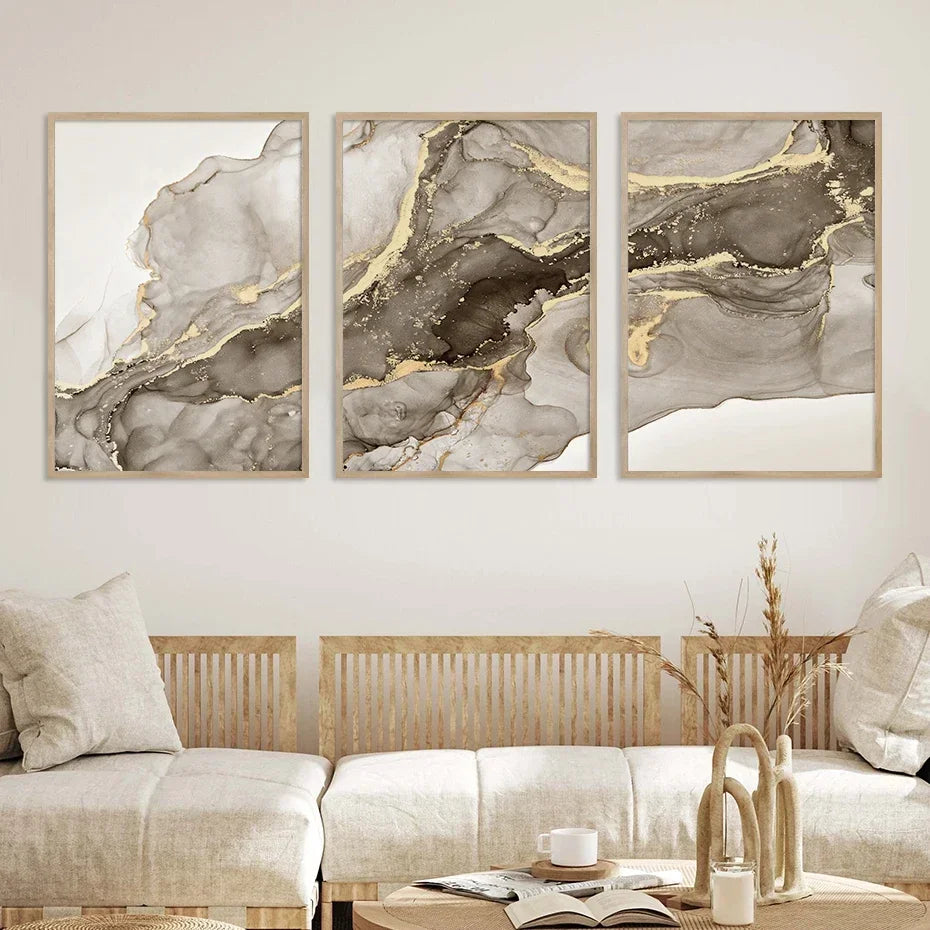 Set of three minimalist abstract canvas prints in grey and taupe tones with gold-effect detailing above a neutral sofa