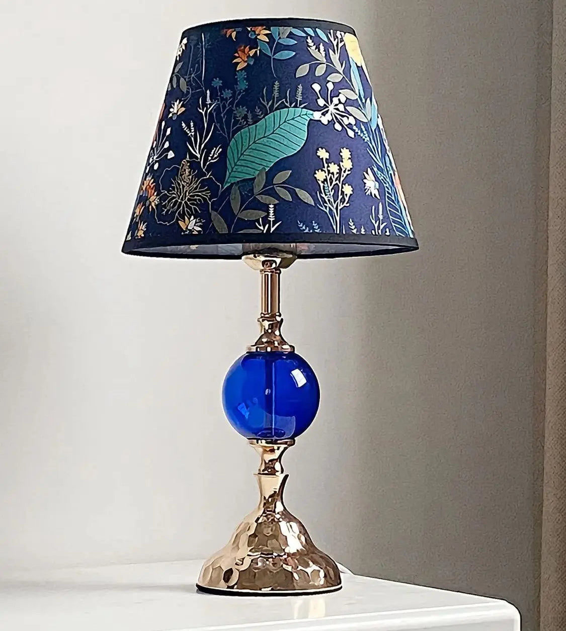 Table lamp with a decorative blue and gold base and a navy floral shade on a white surface.