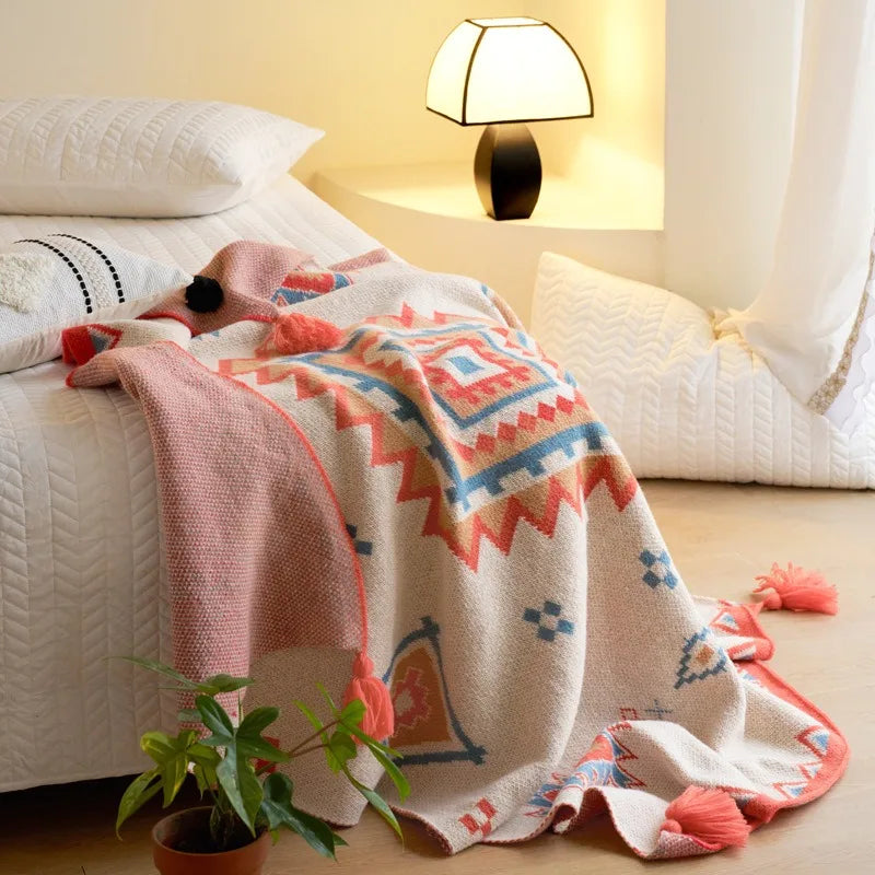 A woven throw blanket with a Southwestern geometric pattern in terracotta red, light blue, and beige, draped over a bed in a warm, modern bedroom setting.