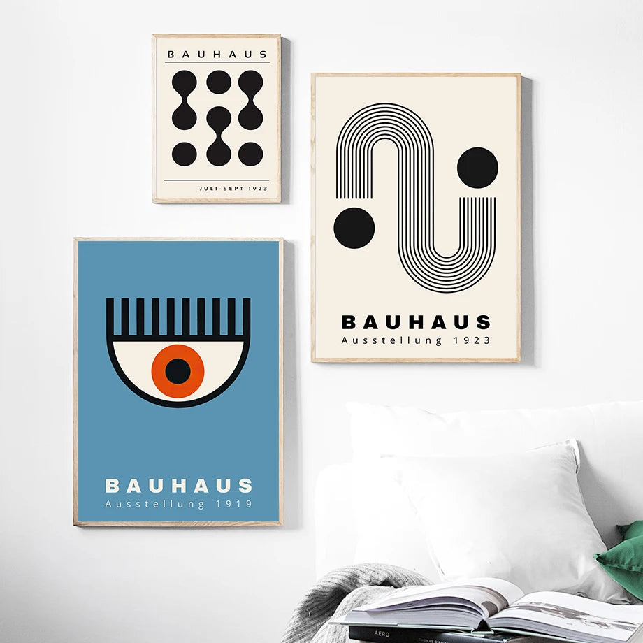 Three Bauhaus art posters on a wall with a bed and books in the foreground.