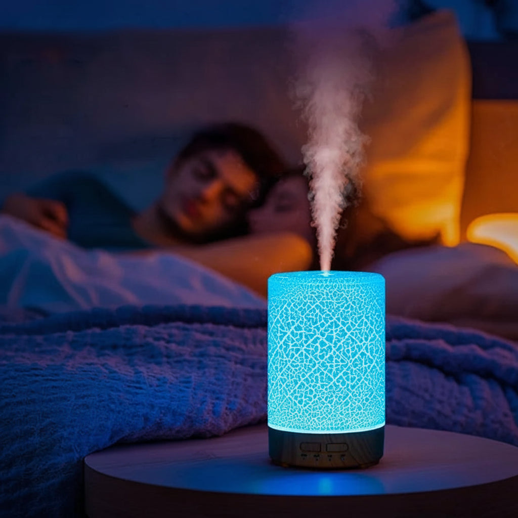 Aromatherapy diffuser emitting mist on a bedside table with a couple lying in bed in the background.