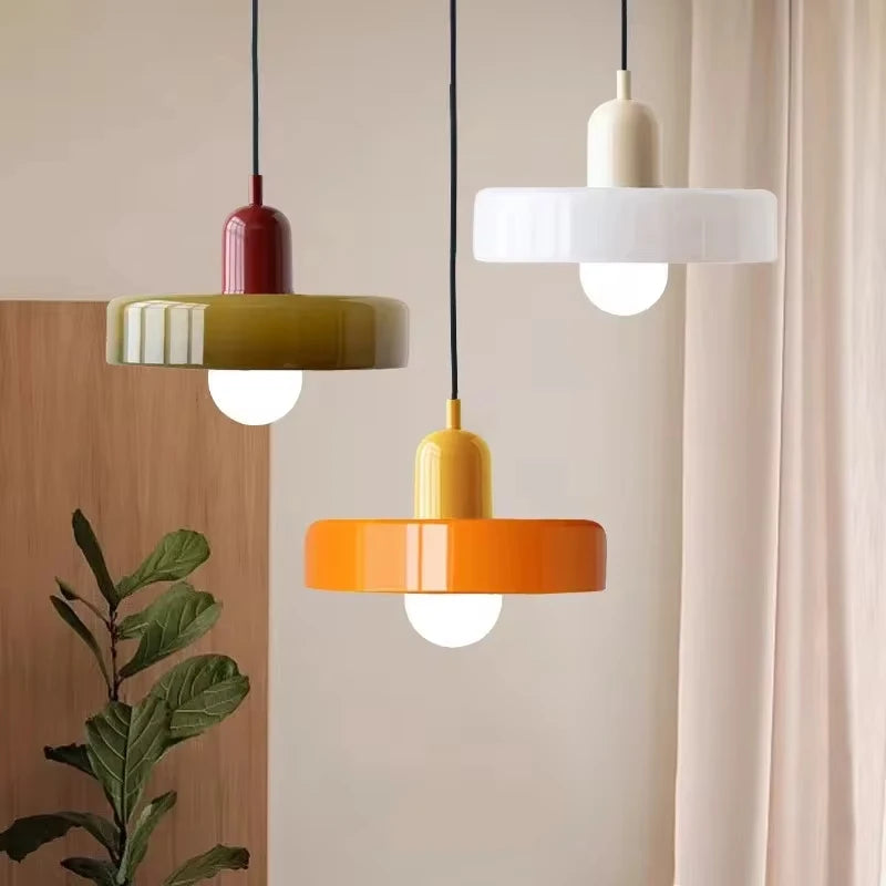 Three colorful pendant lights hanging against a neutral wall with a plant in the corner.