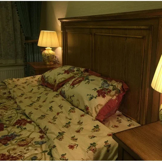 Bed with floral bedding and pillows in a dimly lit room.