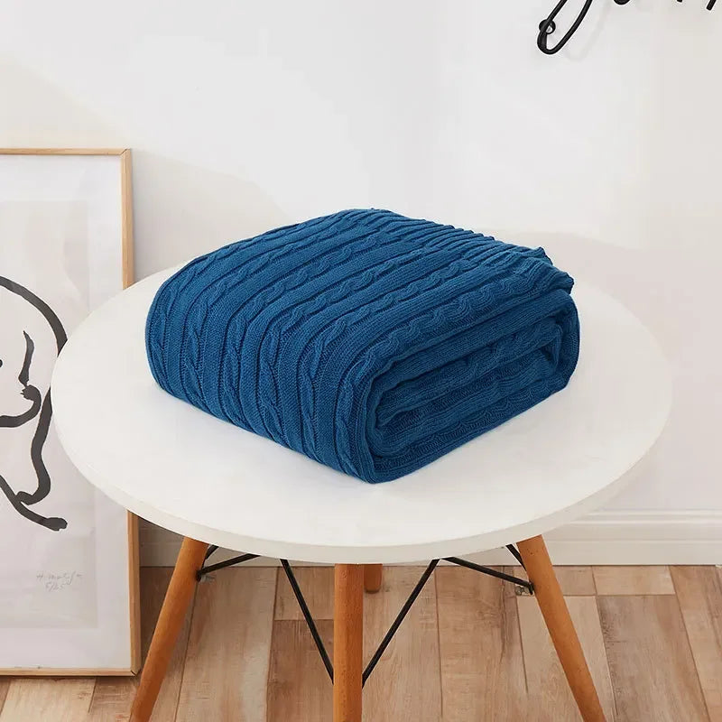 Folded blue blanket on a white round table with wooden legs, against a light-colored wall.