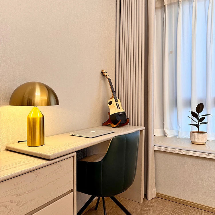 Small home office with a desk, chair, lamp, and guitar against a window.