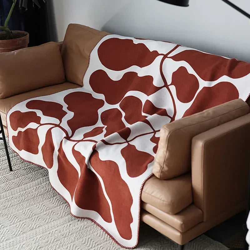 Rust-and-cream abstract jacquard blanket with blanket-stitch edge draped over a sofa.