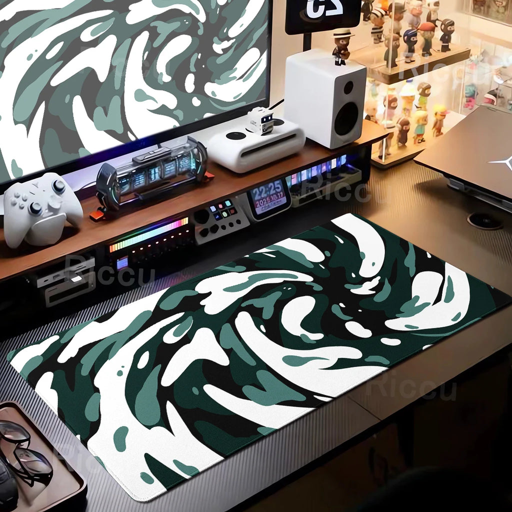 Desk setup with a green and white abstract mouse pad, computer equipment, and decor items.