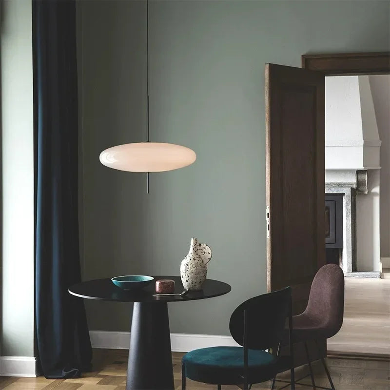 Modern interior with a round table, chairs, and a pendant light against a green wall.