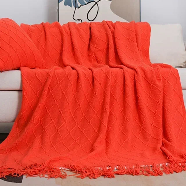 Bright orange-red knit throw with a raised diamond pattern and tassel edge draped over a sofa
