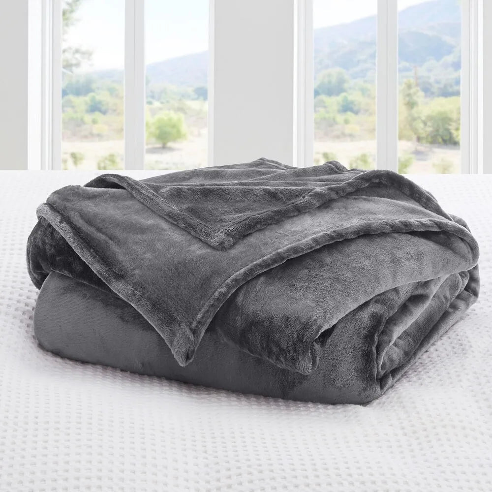 A dark grey plush blanket on a bed with a window view of greenery