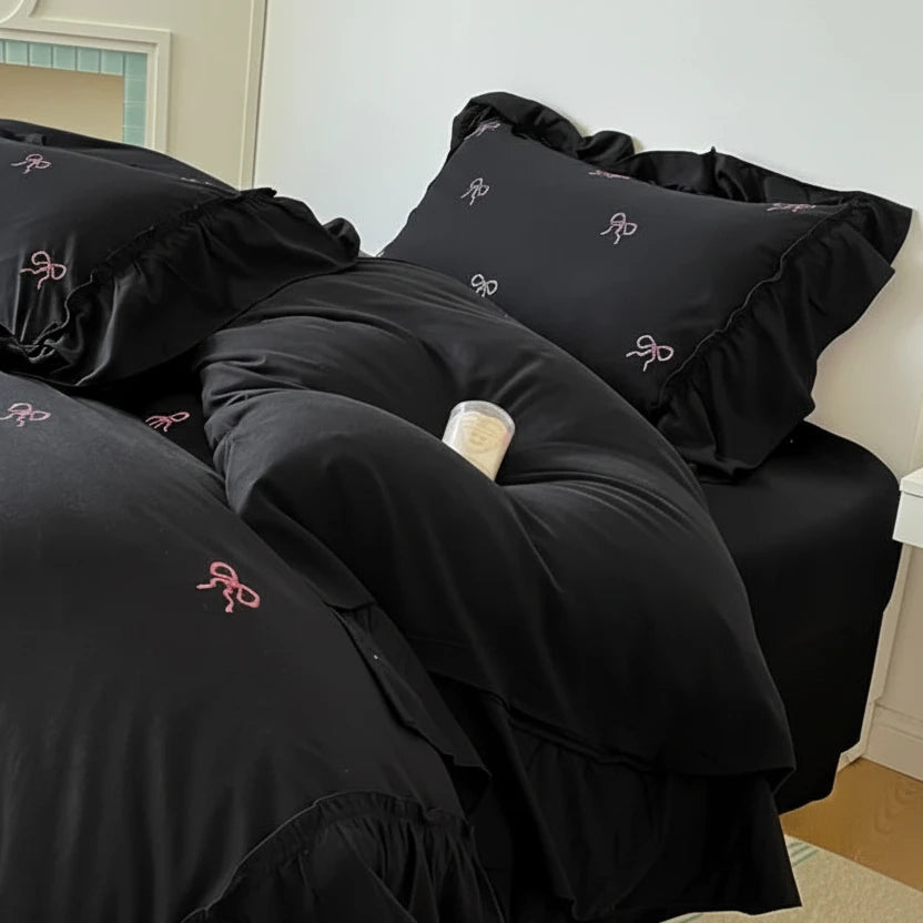 Black bedding set with ruffled edges and embroidered designs on a bed.