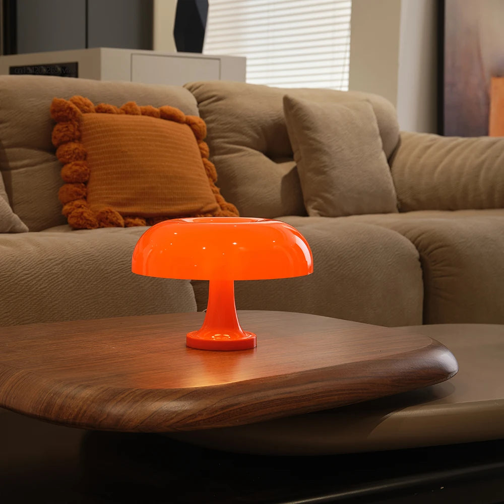 Orange lamp on a wooden coffee table in a living room with a beige sofa and orange pillow.