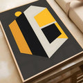 Geometric abstract canvas print featuring angular shapes in gold, grey, and black on a dark charcoal background, set in a natural wood frame.