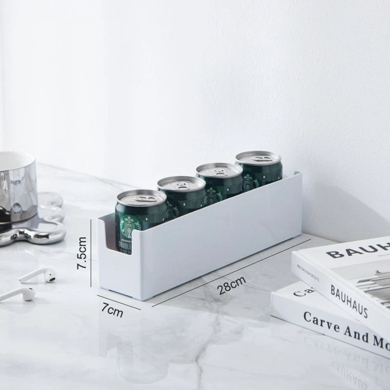 White can holder with four cans on a white surface with books and a coffee pot in the background.