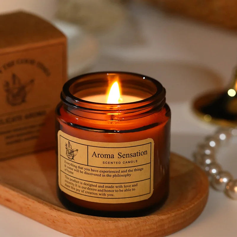 Aroma Sensation scented candle in an amber jar on a wooden coaster with a blurred background.