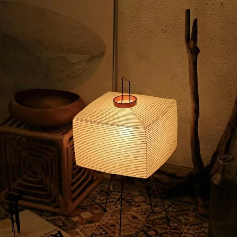 Square woven Japanese floor lamp emitting a warm glow in a dimly lit room.