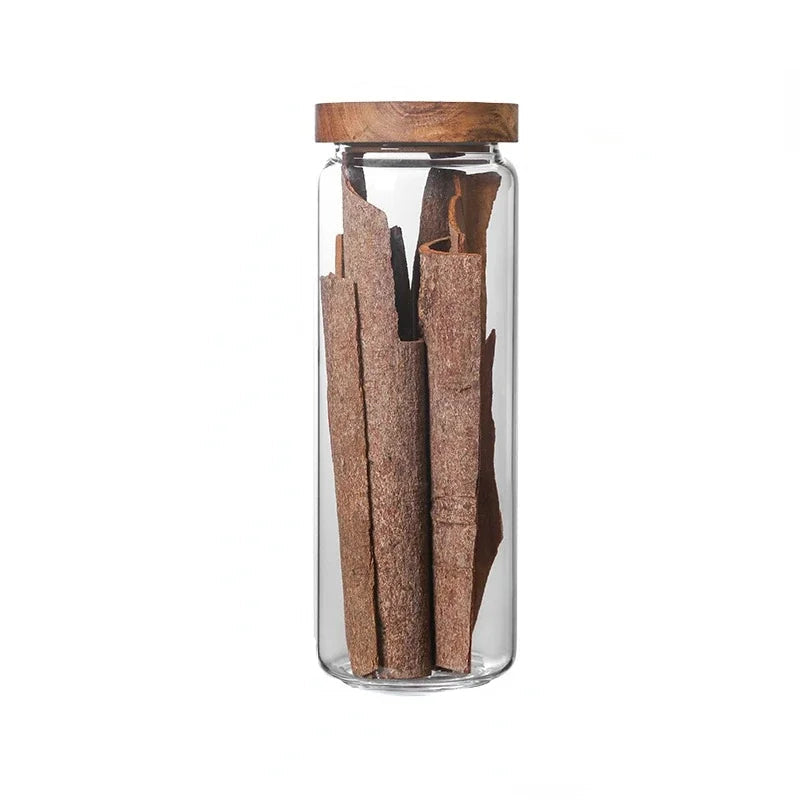 Glass jar with wooden lid containing cinnamon sticks on a white background