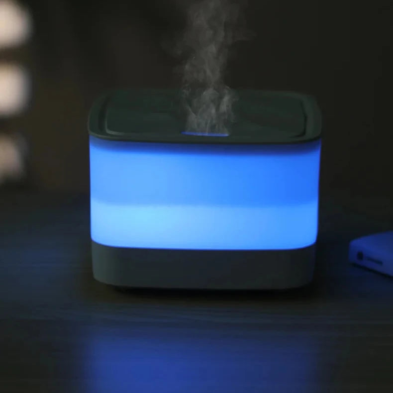 Blue glowing diffuser device emitting mist in a dark setting