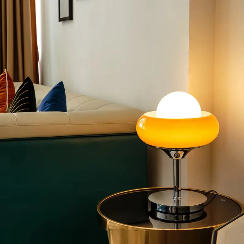 Modern table lamp with a yellow base and white shade on a glass table in a living room.