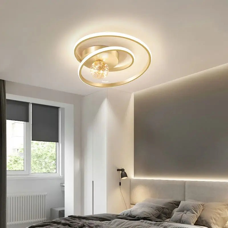 Gold Nordic spiral ceiling light with amber glass globe installed above a modern bedroom with warm ambient lighting