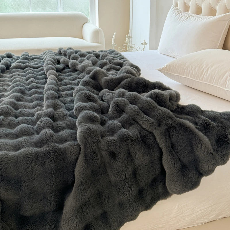 A charcoal fluffy blanket on a bed with a neutral-colored room in the background