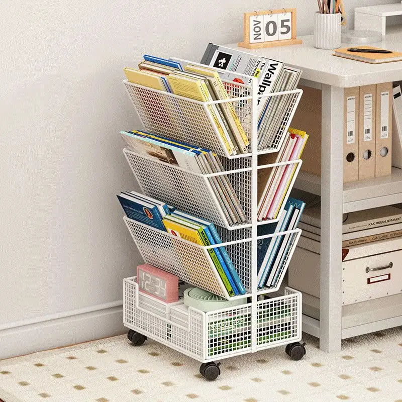 A white metal rolling magazine rack with four tiers and caster wheels, filled with books and magazines in a home office setting next to a desk.