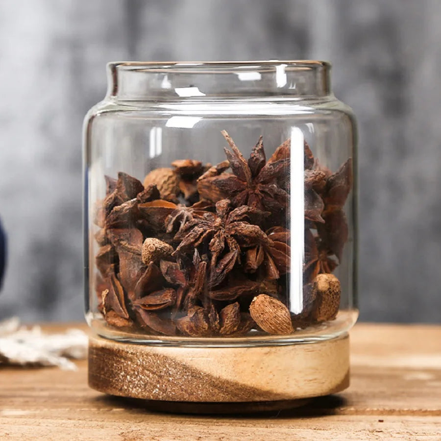 Clear glass jar with wooden base filled with star anise on a wooden surface.