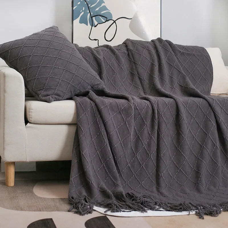 Charcoal grey diamond-patterned knit throw with tassels draped over a sofa with wooden legs