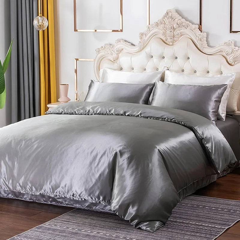 A Grey satin bedding set on a bed with a decorative headboard and yellow curtains.
