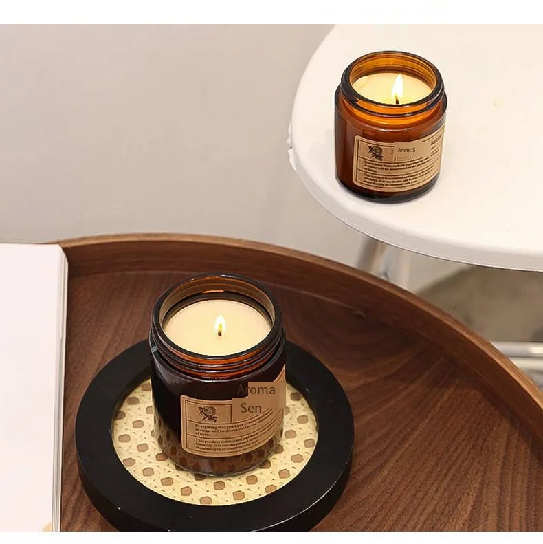 Two aroma glass diffusers with candles on a wooden coaster and on a white surface