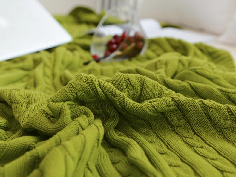 Green knitted blanket on a bed with a blurred glass of water and berries in the background.