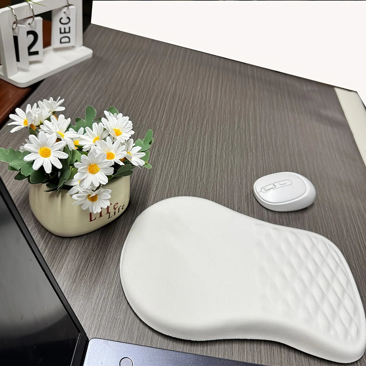 White wrist rest on a desk with a small plant and calendar in the background