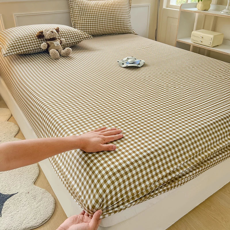 A classic tan and white checkered fitted sheet being tucked into a mattress. The image highlights the deep-pocket elastic fit and smooth Polyester fabric.