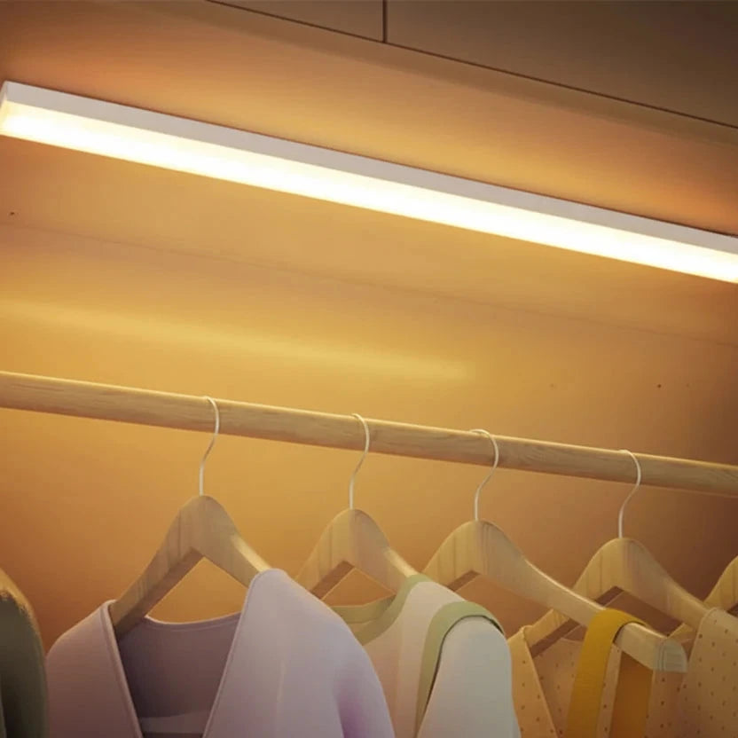 Clothing on hangers under a strip light in a closet