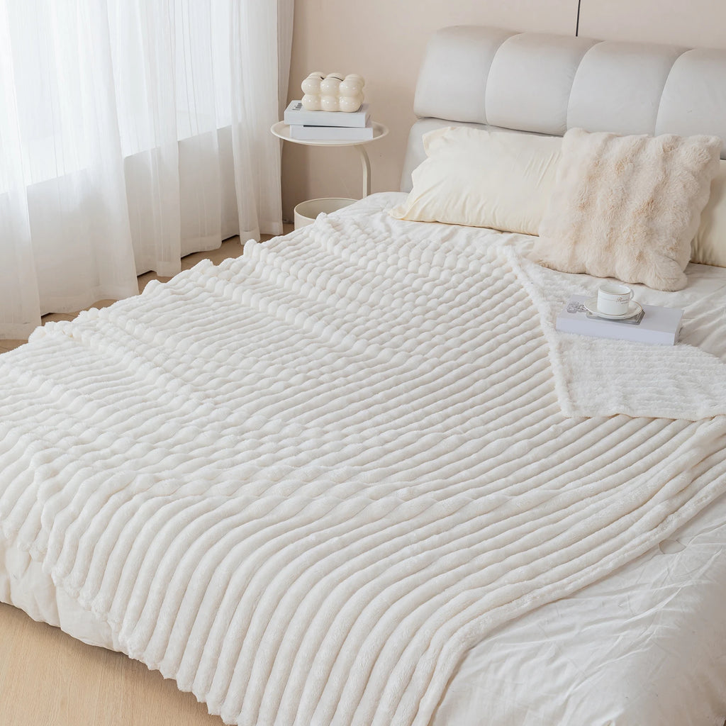 White textured blanket on a bed in a bedroom setting with light curtains and decor.