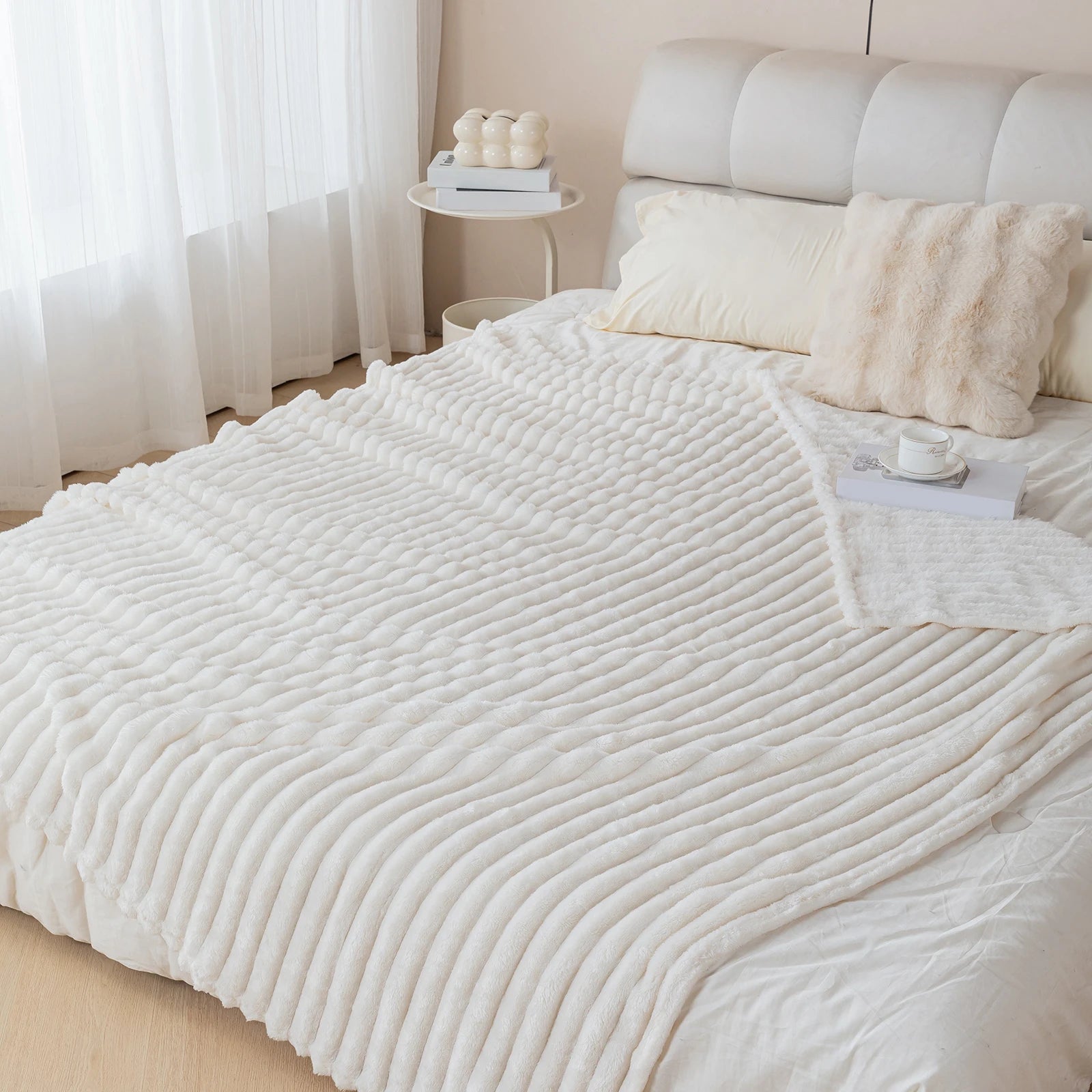 White textured blanket on a bed in a bedroom setting with light curtains and decor.