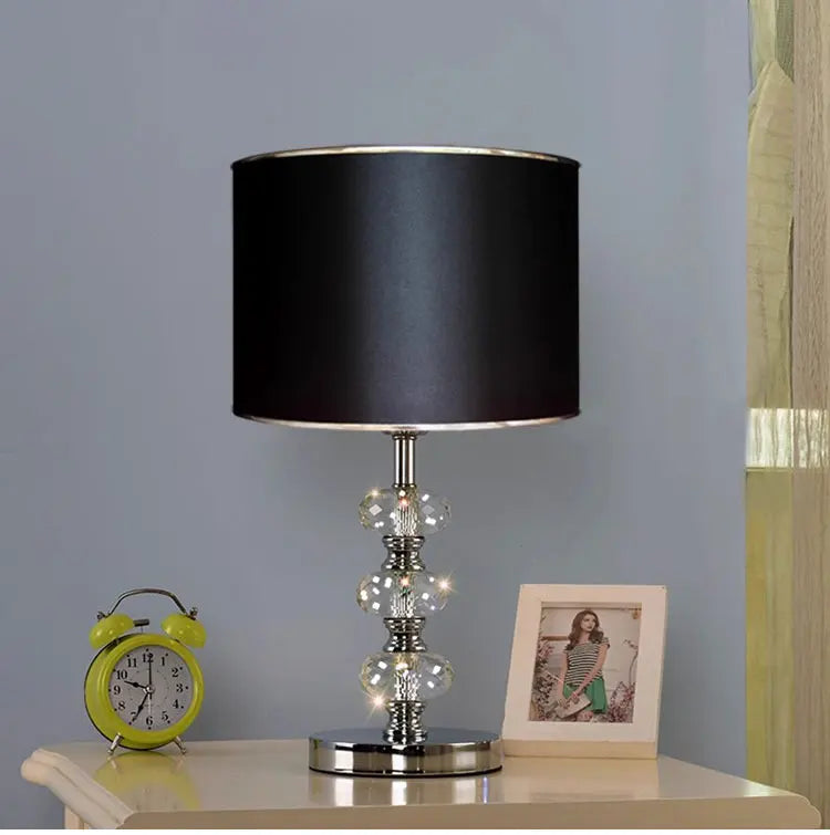 table lamp with a solid black cylindrical shade and a triple-stacked crystal base on a nightstand.