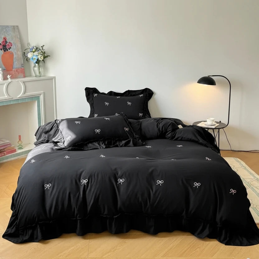 Full view of the Midnight Noir duvet set featuring a black base with white embroidered bows and elegant ruffled edges in a minimalist bedroom setting.