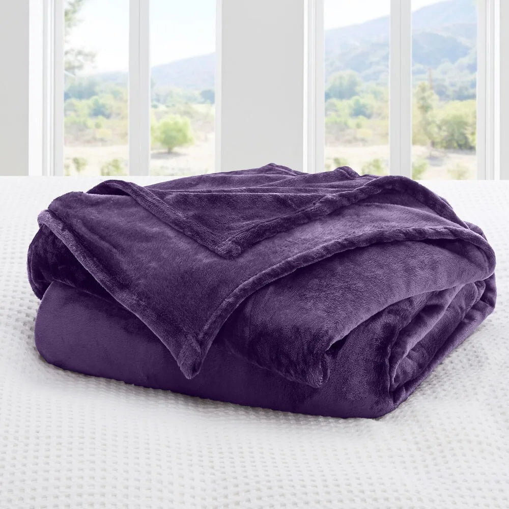 A deep purple blanket on a bed with a window view of greenery