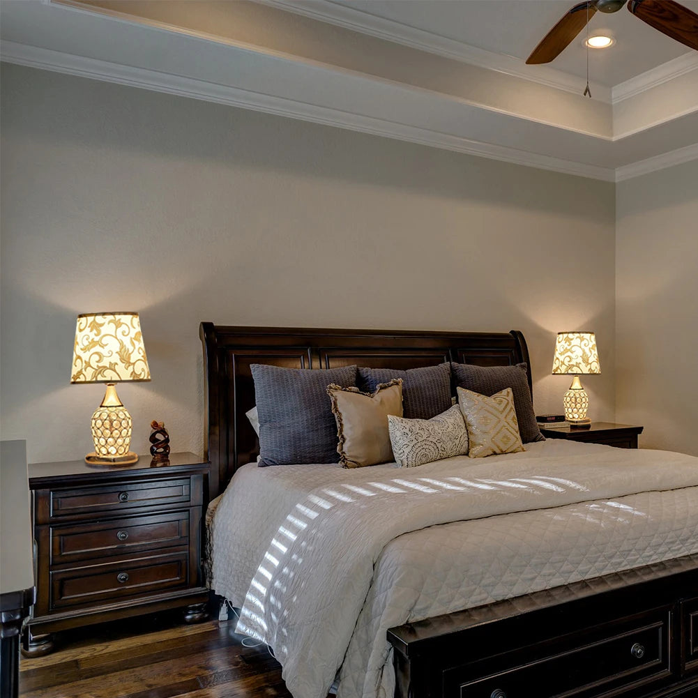 Gold crystal-lattice bedside lamp with gold scrollwork fabric shade on a nightstand either side of a double bed