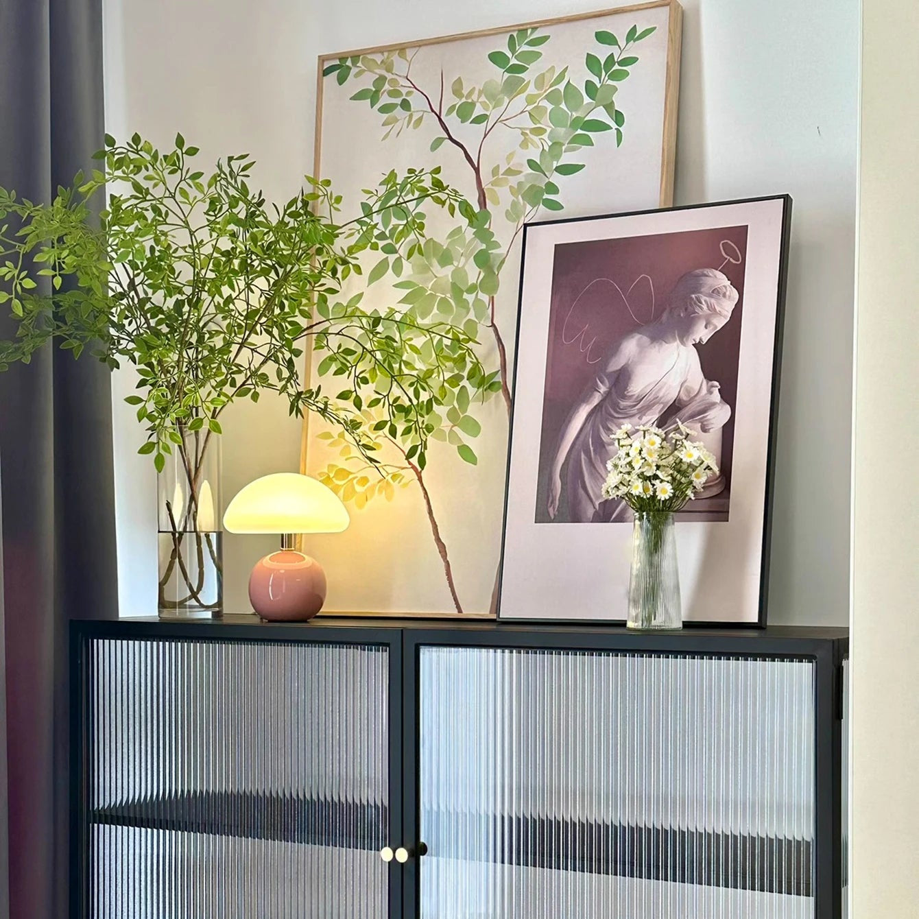 Decorative shelf with plants, lamp, and framed pictures in a room.