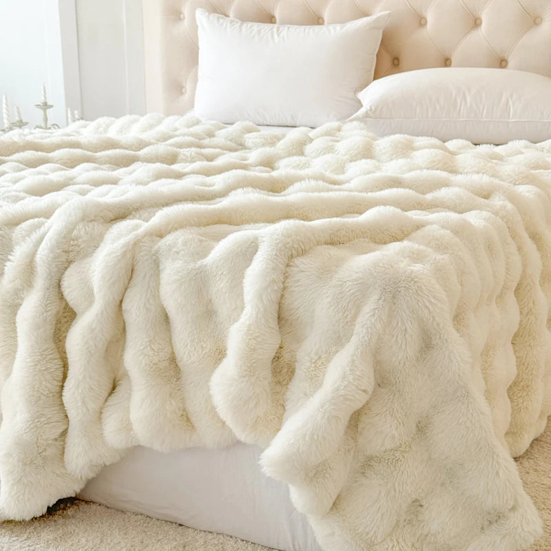 Cream-colored faux fur blanket draped over a bed with white pillows.