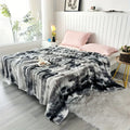 A greyish, black and white tie dye blanket on a bed with pink pillows in a bright bedroom.