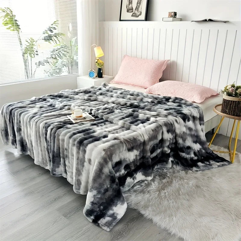 A greyish, black and white tie dye blanket on a bed with pink pillows in a bright bedroom.