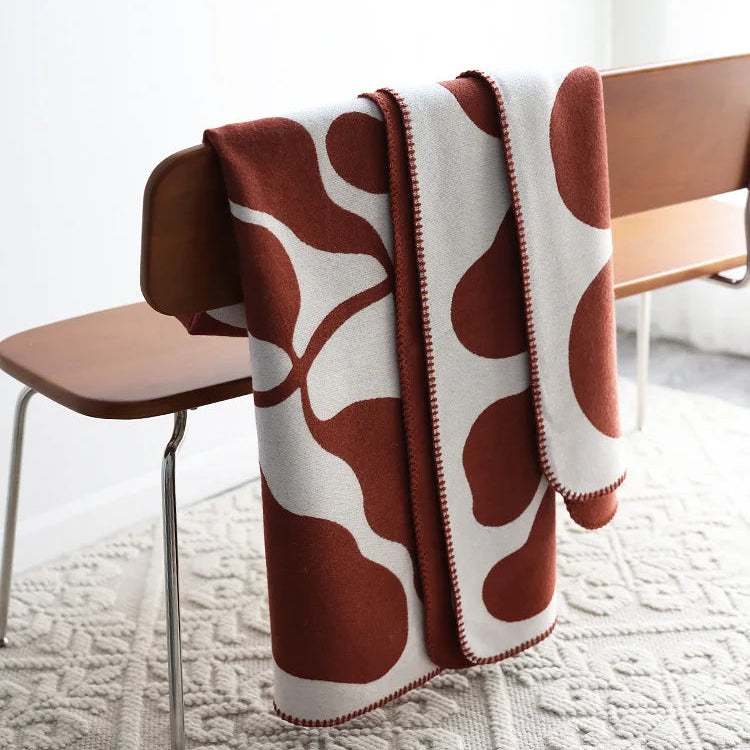 Rust and cream abstract jacquard blanket with blanket stitch edge draped over a wooden chair on a textured cream rug