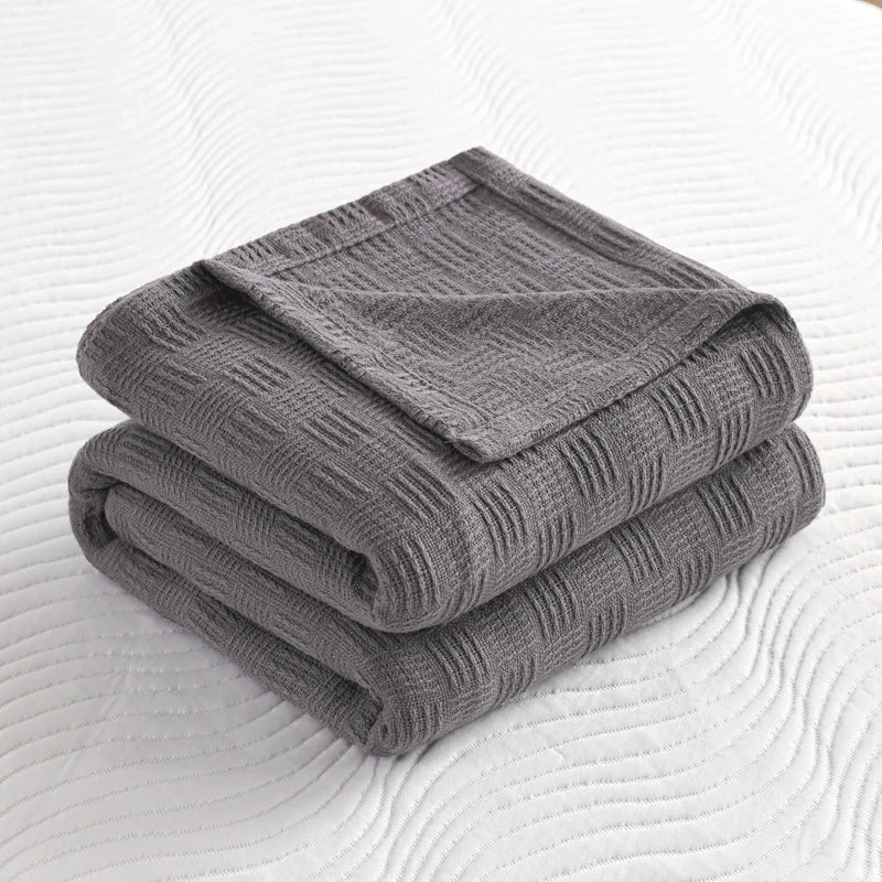 Folded charcoal grey knit throw with structured weave detail on white quilted surface