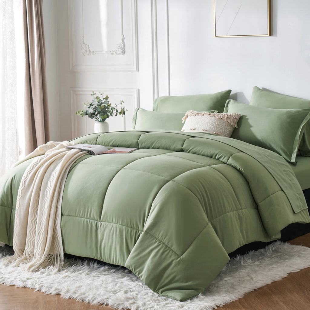 Green comforter set on a bed in a bright bedroom with a plant and lamp.